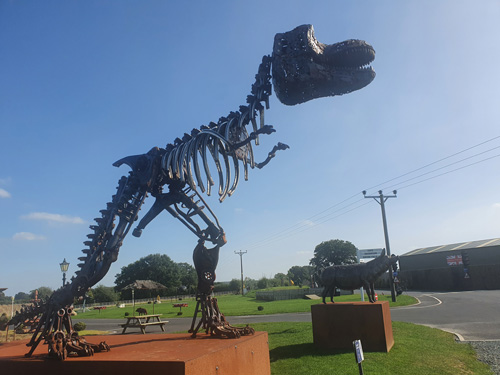  large, intricately detailed metal sculpture of a T-Rex skeleton at the British Ironwork Centre, displaying the dinosaur's massive frame and sharp teeth.