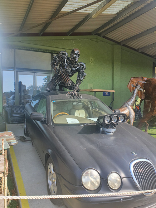 A creative metal sculpture of the Terminator character on a car at the British Ironwork Centre, depicting the iconic figure in a dynamic pose, with intricate details and craftsmanship.