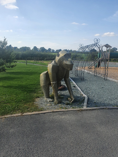 A detailed metal sculpture of a large monkey at the British Ironwork Centre, capturing its playful expression and lifelike features, displayed prominently in the outdoor exhibition area.