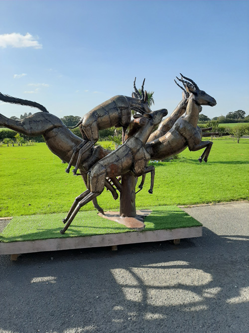 A captivating metal sculpture of a house at the British Ironwork Centre, adorned with detailed figures of stags leaping in motion, displayed in the outdoor exhibition area.