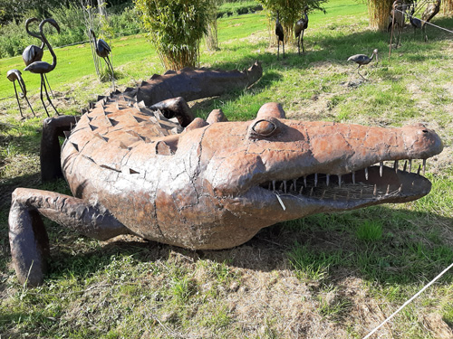 A unique metal sculpture of a house at the British Ironwork Centre, featuring a creatively crafted crocodile as part of its design, displayed in the outdoor exhibition area.