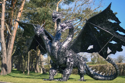 A majestic metal sculpture of a large dragon at the British Ironwork Centre, featuring intricate scales, fearsome claws, and a powerful stance, displayed prominently in the outdoor exhibition area.