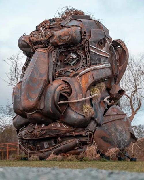 A monumental metal sculpture of a giant's head at the British Ironwork Centre, displaying intricate facial features and detailed craftsmanship, showcased in the outdoor exhibition area.