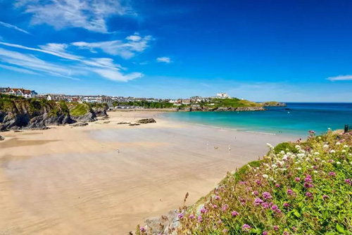 Enjoy a stunning view from Great Western Beach in Newquay, Cornwall. Admire the expansive golden sands, rolling waves, and scenic coastal cliffs of this popular beach destination.