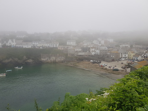 Experience the enchanting view over Port Isaac bay shrouded in mist. Admire the ethereal beauty of the historic village and its serene coastal scenery enveloped in a mystical atmosphere.