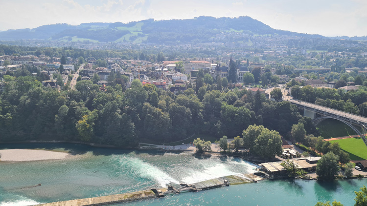 Bern Cathedral with a serene river, vibrant trees, and majestic architecture in the backdrop