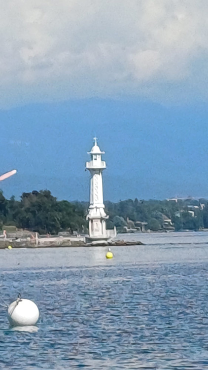 Lighthouse on a rocky shore by a lake, with a clear sky and clouds above