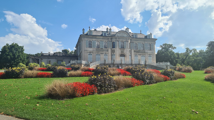 The History of Science Building, featuring numerous windows, set outdoors amidst landscaped gardens with grass, plants, and flowers