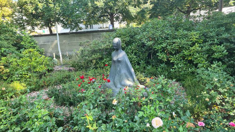 Statue surrounded by lush greenery and colorful flowers in Rosengarten Bern