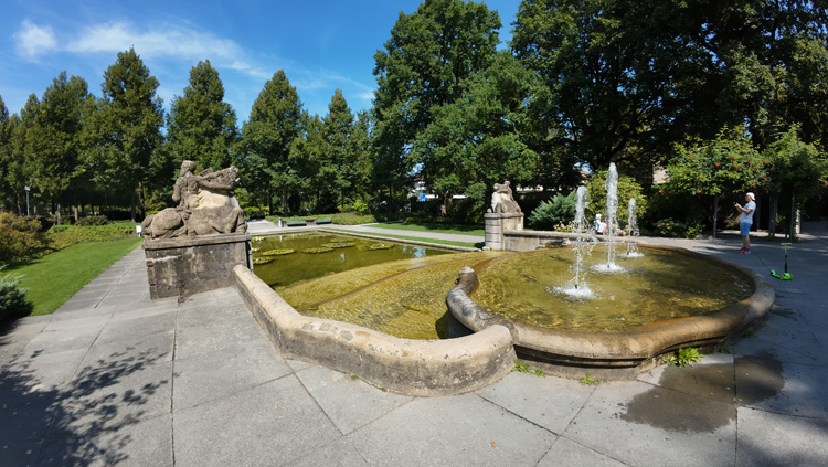 Fountain surrounded by statues, lush greenery, and vibrant flowers in Rosengarten Bern