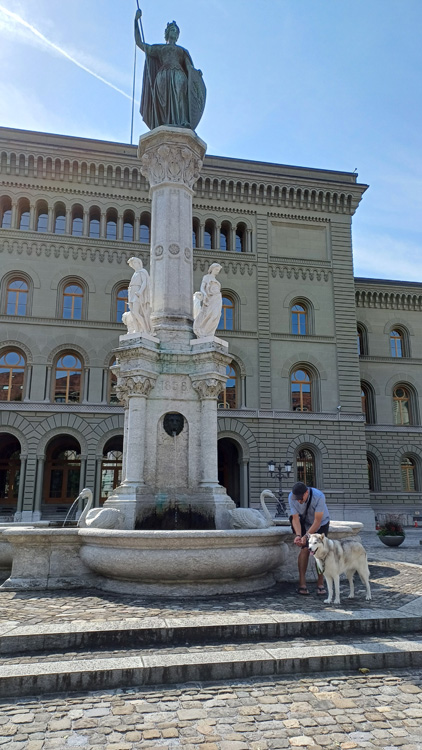 Man and woman standing beside the Bernrunnen Monument with a statue of a man on horseback, set in a town square with classical architecture