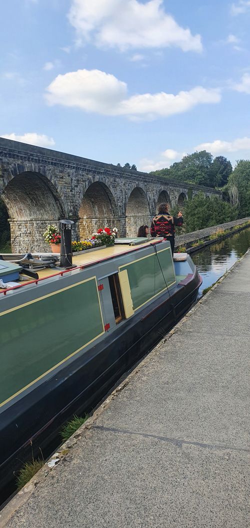 A scenic view of Pontcysyllte Aqueduct, a UNESCO World Heritage site in Wales, featuring a canal boat crossing the impressive structure, with lush greenery and clear blue sky in the background.