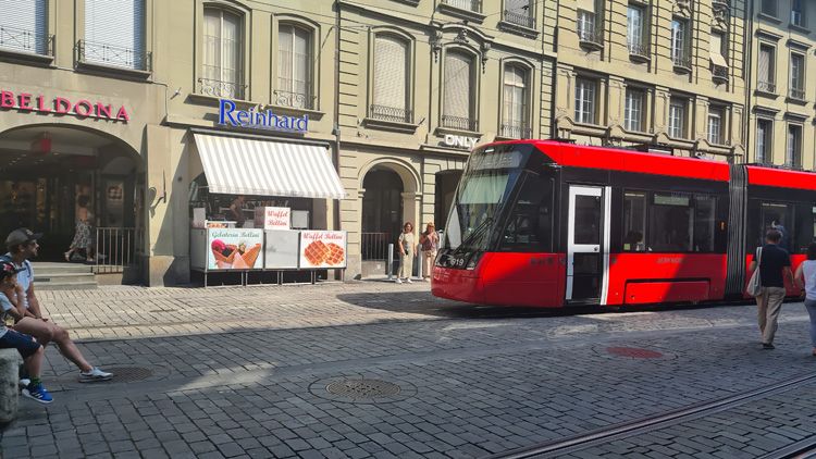 Red trolley on a cobblestone street in Bern surrounded by historic buildings