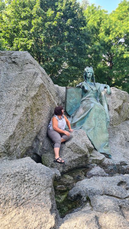 Lady posing beside the Universal Post Monument in Bern, surrounded by trees and rocky terrain on a hiking trail
