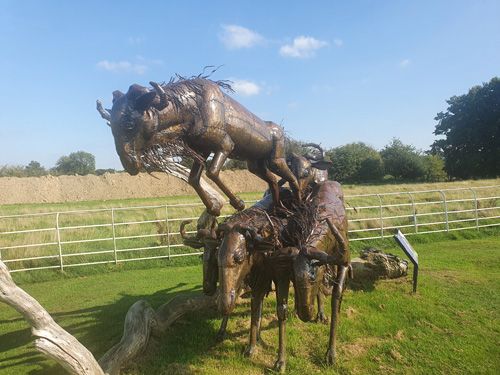 A dynamic metal sculpture at the British Ironwork Centre depicting wildebeests in mid-leap, artfully crafted to appear as if they are jumping over each other in a lively scene.