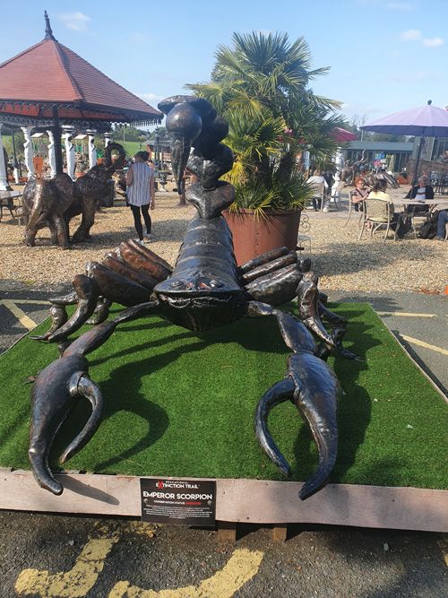 A striking metal sculpture of a large scorpion at the British Ironwork Centre, showcasing its intricate details and menacing appearance, displayed prominently in the outdoor exhibition area.