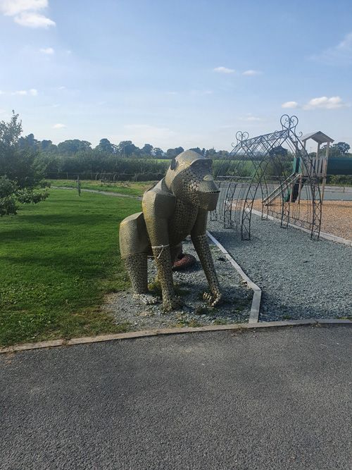 A detailed metal sculpture of a large monkey at the British Ironwork Centre, capturing its playful expression and lifelike features, displayed prominently in the outdoor exhibition area.