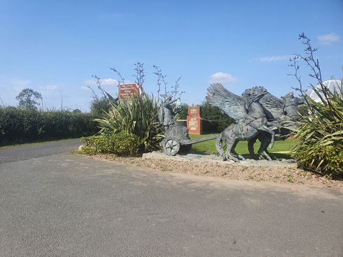A striking metal sculpture at the British Ironwork Centre, depicting a flying horse with outstretched wings pulling an ornate cart through the air.