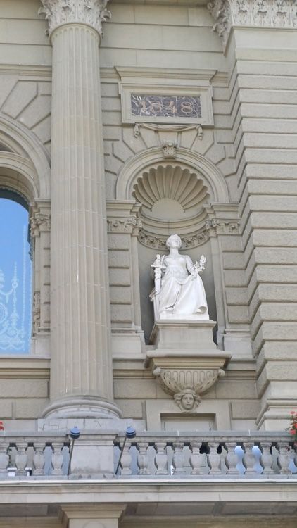Detailed statue within Bern Parliament, framed by intricate molding and facade elements, with windows highlighting the structure’s charm