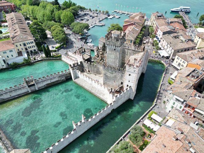 Aerial view of Castello Scaligero di Sirmione, a historic fortified castle surrounded by water in a scenic, picturesque setting.