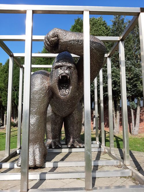 A metal sculpture of a house at the British Ironwork Centre, creatively incorporating a gorilla in a cage as part of its design, displayed in the outdoor exhibition area.
