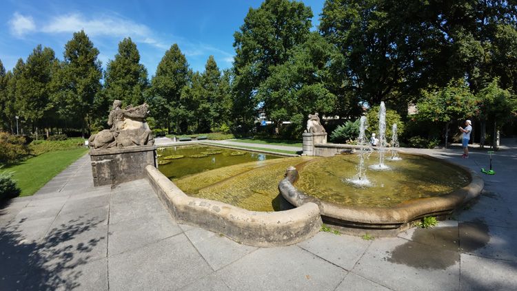 Fountain surrounded by statues, lush greenery, and vibrant flowers in Rosengarten Bern