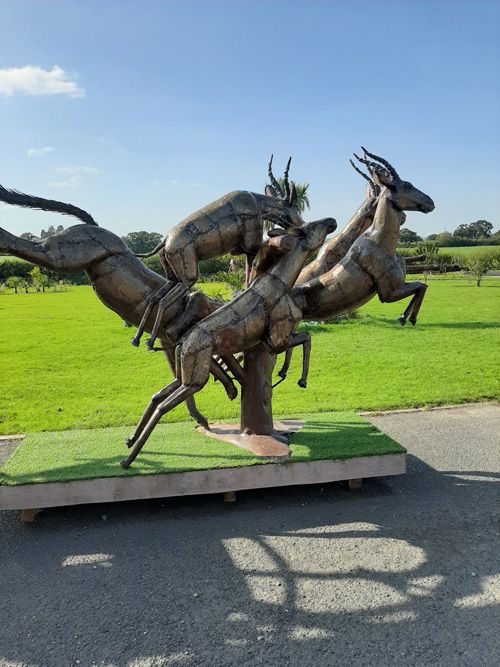A captivating metal sculpture of a house at the British Ironwork Centre, adorned with detailed figures of stags leaping in motion, displayed in the outdoor exhibition area.