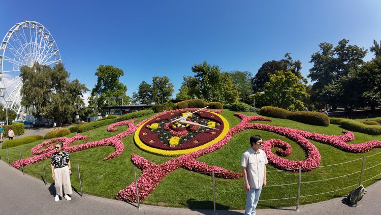 People standing in a park by a colourful flower clock, surrounded by lush plants and trees