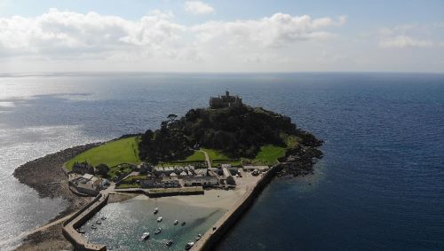 Experience the breathtaking aerial view of National Trust - St Michael's Mount. See the historic island castle, its gardens, and the surrounding Mount's Bay from a stunning bird’s-eye perspective.