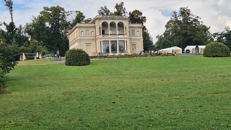 The History of Science Building, featuring numerous windows, set outdoors amidst landscaped gardens with grass, plants, and flowers